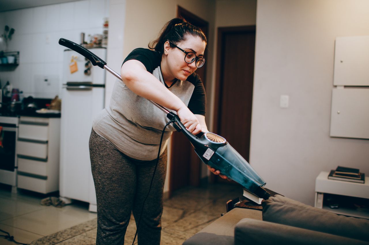 about-01 A woman vacuuming a couch in a cozy living room setting, emphasizing daily housework.
